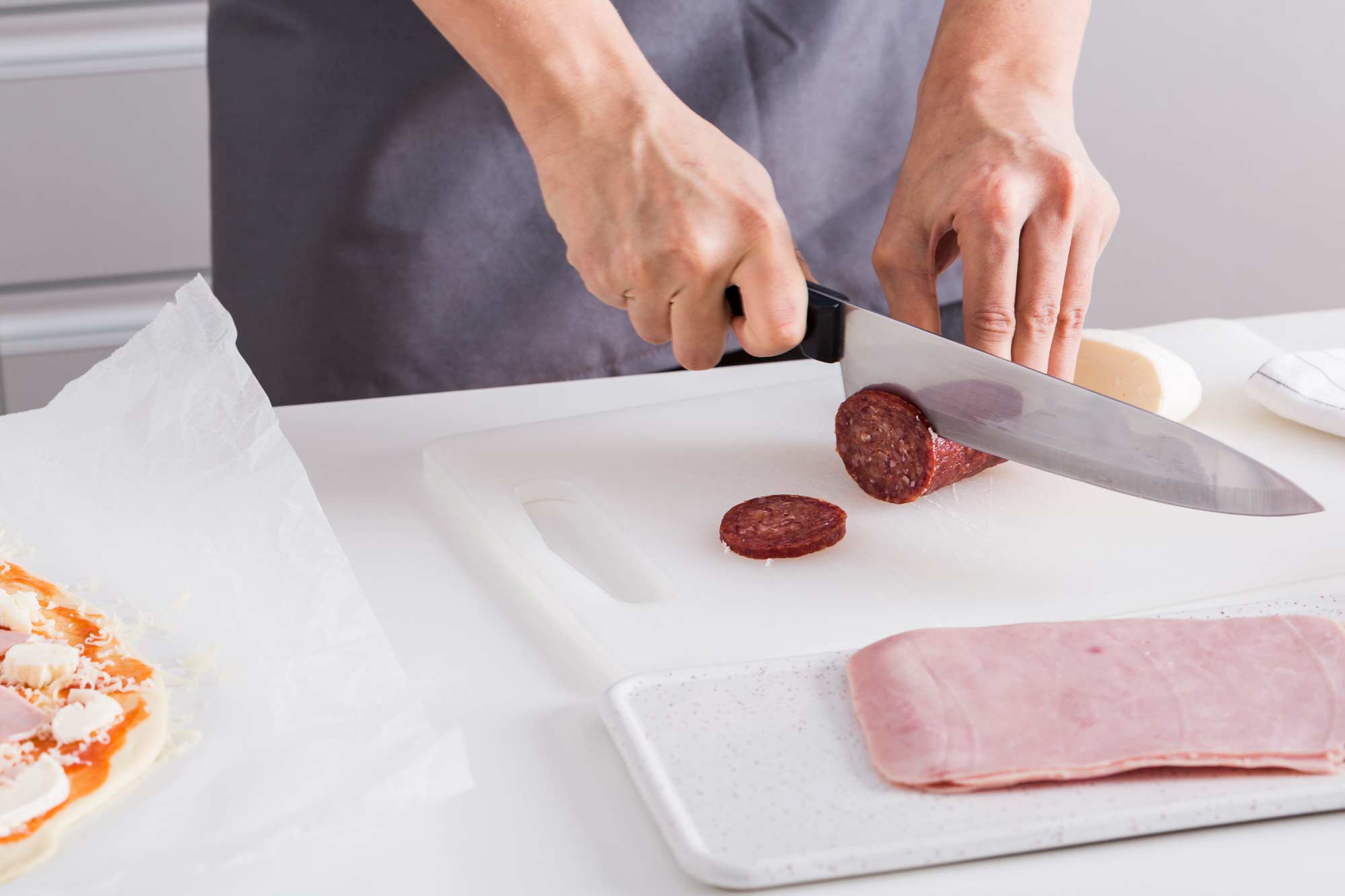 Persona cortando embutido sobre tabla de cortar en una cocina